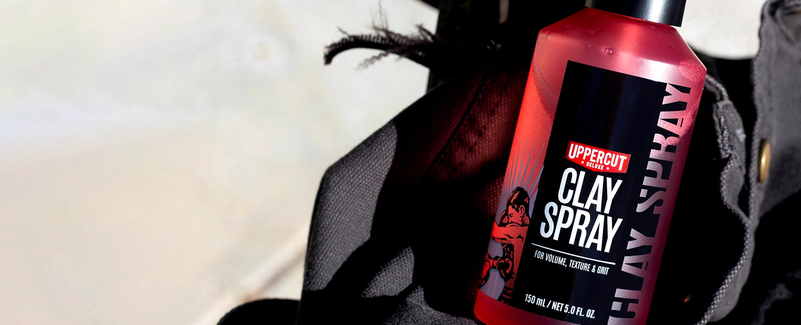 Uppercut Deluxe Clay Spray placed in a heavy canvas bag on a blurred background