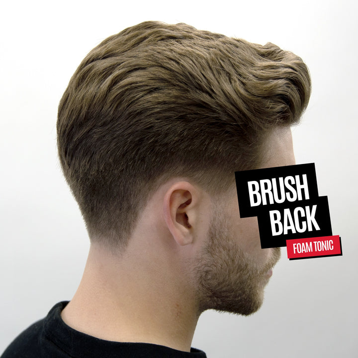 Side profile of a man with styled, voluminous brown hair showing the product in use. A black and red graphic overlay reads 'BRUSH BACK FOAM TONIC'.